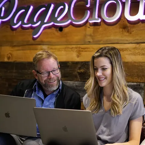 Two colleagues smiling at their laptops under the Pagecloud sign