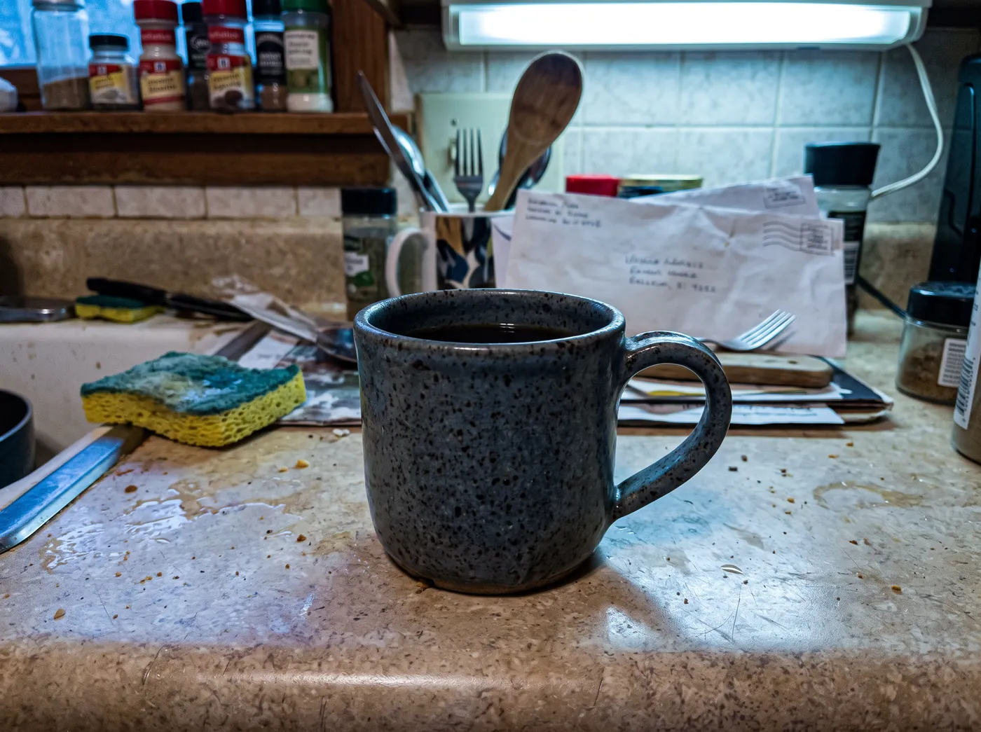 Une photo rapide au téléphone d’une tasse en grès moucheté sur un comptoir de cuisine encombré.